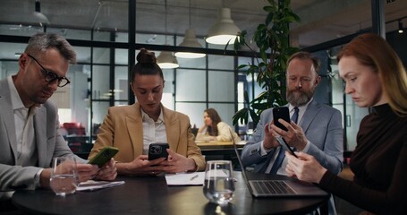 A group of stylish business people use mobile phones while sitting at the same desk in the office