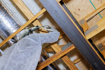 Worker in protective clothing is spray foam insulation at basement as part of home renovation...