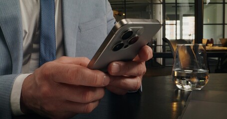 A man uses mobile phone sitting at a desk in an office. Close-up of his hands, unrecognizable person