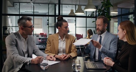 A man shouts at his colleagues and throws documents at them at a business meeting in the office