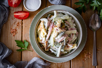 A hearty lunch: A salad with ham, vegetables, and mayonnaise on a green plate on a wooden table. Top view. Close-up
