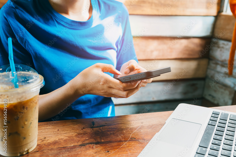 Poster woman using smartphone. person using smartphone while sitting at a wooden table with coffee and lapt