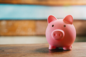 Cute pink piggy bank on wooden surface with blurred blue background, symbolizing saving and...