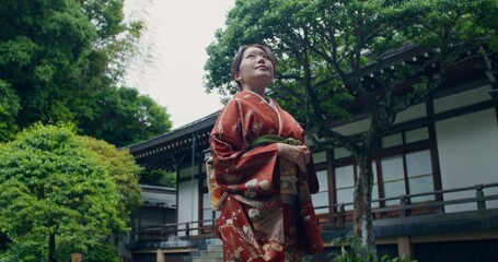 An elegant Japanese woman in national clothes stands near a traditional Japanese house on a summer...