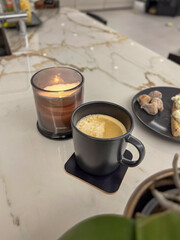 Cozy coffee cup beside a lit candle on a marble countertop, with a plate of pastries, creating a warm and inviting atmosphere for relaxation and enjoyment