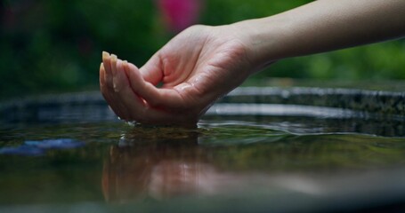 A woman's hand touches the water in the font in the open air. Close-up, unrecognizable person