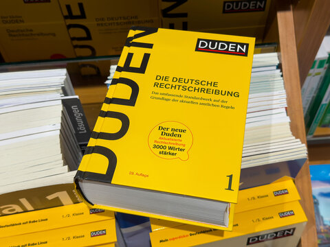 Villach, Austria - July 01, 2025: Duden dictionary on display in bookstore, showcasing vibrant yellow cover and stacked books, representing German language and grammar reference