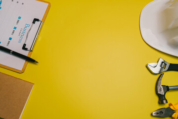 Real estate concept. Business workspace with tools, clipboard, and safety helmet on vibrant yellow background for construction or project planning themes