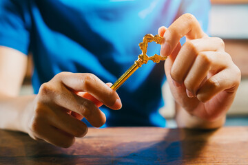 Golden Key Held by Person with Blue Shirt in Bright Indoor Setting Suggesting Opportunity and...
