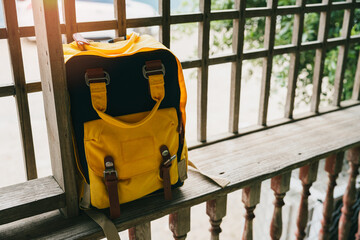 Yellow travel bag. Stylish yellow backpack resting on wooden railing in serene outdoor setting with...