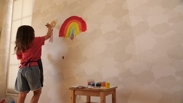 Young girl painting rainbow on wall in playroom