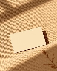 Blank beige card on textured brown fabric, shadow of leaves, mockup for design