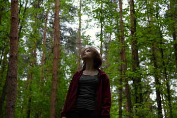 Beauty face emotional woman looking up on a green pine trees in the forest on sun spring weather. Girl walking in fashion dress, breath fresh air. Closeup portrait.  Focus on facial expressions