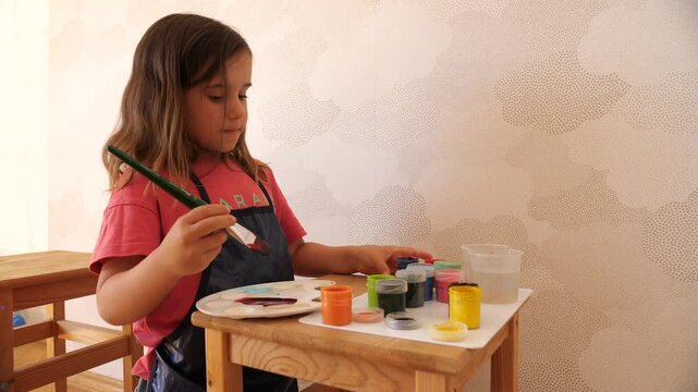 Young girl painting with tempera colors on a wooden table