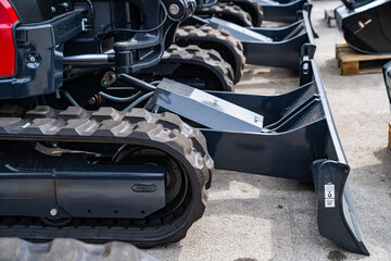 Crawler track system and metal blade of compact construction equipment lined up outdoors showcasing...