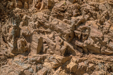 Detailed close-up of a rugged rock face. showcasing intricate layers and fractured textures in...