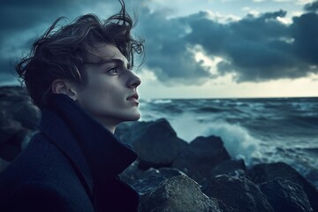 A young man with windblown hair gazes pensively at a stormy sea, evoking a sense of solitude and contemplation.