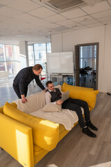 Two Caucasian men discussing work on a laptop while sitting on a sofa. Modern office. 