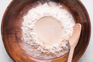 Overhead view of bread dough being mixed in a wooden bowl, top view of homemade bread dough in a...