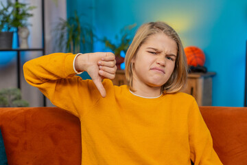 Dislike. Upset teenager boy gives thumbs down while sitting at home on sofa with an frowning...