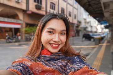 Fototapeta premium Beautiful Asian woman smiling sweetly taking a selfie using the camera. Happy woman in the city.