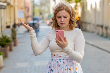 Redhead young woman in long dress use smartphone typing browsing loses becoming surprised sudden...