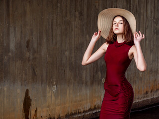 Young girl in luxurious red dress and large hat in a vogue style look posing standing in water...