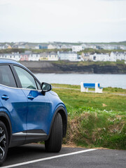 Stylish blue car is standing in car park by the ocean with view on stunning nature scenery with...