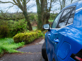 Blue car is back in a back yard of and old house with view on green rural country side area with lots of greenery which provides lots of fresh healthy air. Living in good ecology place concept.