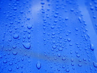 The image is of a blue surface with many small drops of water on it. The drops are scattered all...