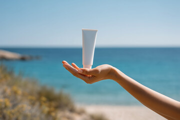 A tube of sunscreen. Sunscreen in hand against the beach in the background.