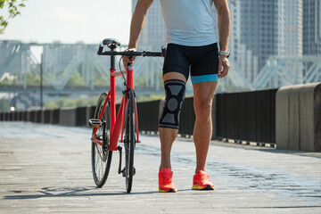 Cyclist walks with bandage on knee at public park. Unhappy cyclist with knee pain and injury...
