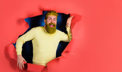 Happy bearded man breaking through paper wall. Handsome male in casual sweater with yellow dyed...