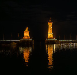 The entrance to Lindau harbor with the illuminated lighthouse and lion monument at night, seen from the Christmas market.