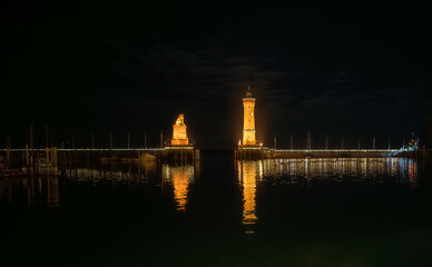 The entrance to Lindau harbor with the illuminated lighthouse and lion monument at night, seen from...