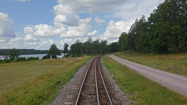 Curved dual gauge track through Swedish countryside on a sunny summer day. Surrounded by fields, forest and clouds in a blue sky