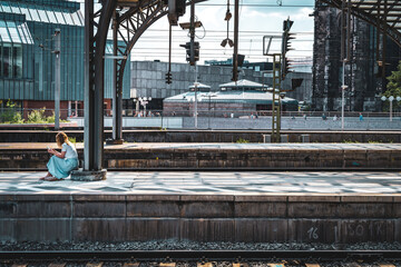 A woman is sitting at Cologne railway station, waiting for a train.