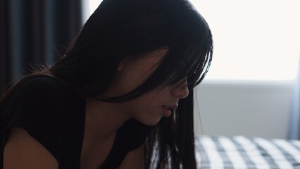 Woman with dark hair falling across face, gazing pensively inside shadowy bedroom
