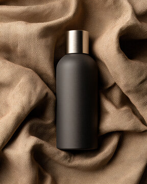 Charcoal gray cosmetic bottle with brushed metal cap on kraft paper and linen textile, soft side lighting, minimal and modern