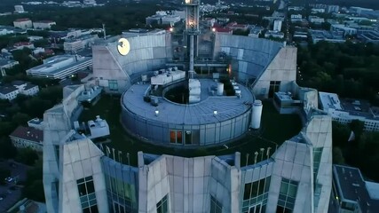 An aerial shot showcases the top of a tall building, with a cityscape sprawling into the horizon under a muted, dusky sky - Powered by Adobe