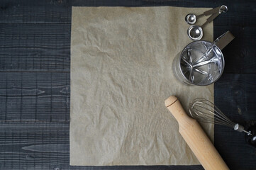 Top view of baking tools on dark wooden table with parchment paper stirring stick flour sieve and...