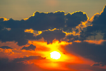 Fototapeta premium Dramatic sunset with a silhouetted cloud partially covering the sun. The warm gradient of orange and yellow tones creates a stunning contrast against the darker sky.