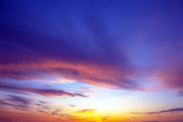 Fototapeta premium Dramatic sunset sky featuring golden, fiery clouds against a deepening blue background. The rich colors and dynamic cloud formations create a stunning natural display.