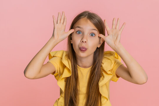 Young child girl sticks out tongue teasingly while making goofy faces cheerful grimaces into camera. School kid isolated on pink background, acting silly and playful with joyful gestures and emotions