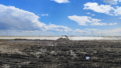 Industrial construction site with muddy tire-tracked ground and vibrant blue and cloudy sky....