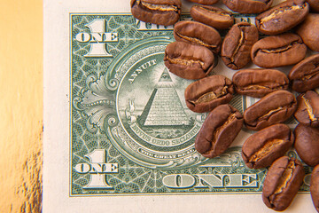 Roasted coffee beans cascade over a stack of U.S. dollar bills on a golden backdrop, representing...