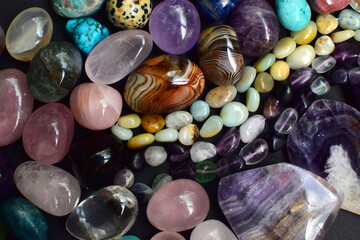 Background of beautiful natural colored semi-precious stones and beads of fluorite and amazonite. Purple amethyst, agate, labradorite, jasper, kyanite, lapis lazuli on a dark background close-up.