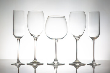 A sleek lineup of five elegant, empty wine glasses with long stems, reflecting on a glossy surface against a soft gray background, perfect for dining or event themes.