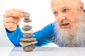 Enthusiastic older man smiling widely while engaged in building a stack of assorted stones,...
