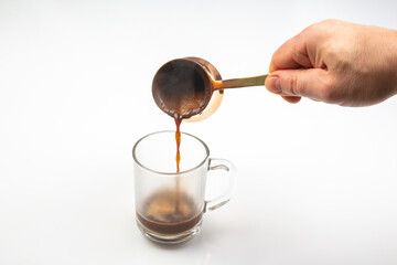 Turkish coffee flows from a traditional cezve into a clear glass cup, capturing the thick, foamy...